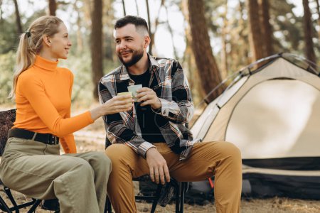 Téléchargez les photos : Couple boire du thé près de leur tente dans la forêt - en image libre de droit