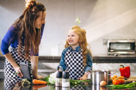 Téléchargez les photos : Mère et fille avec tablette cuisson dans la cuisine - en image libre de droit