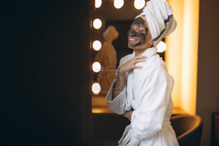 Téléchargez les photos : Femme avec masque noir sur le visage en peignoir dans la salle de bain - en image libre de droit