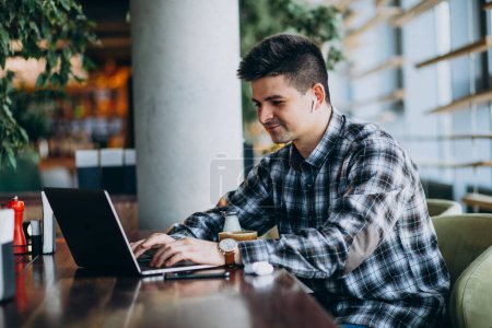 Téléchargez les photos : Jeune homme d'affaires beau utilisant un ordinateur portable dans un café - en image libre de droit