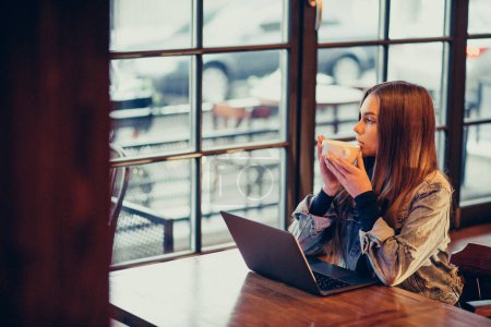 Photo for Young woman studying on laptop and drinking coffee in bar - Royalty Free Image