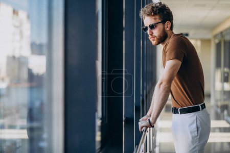 Téléchargez les photos : Jeune homme beau debout près de la fenêtre à l'aéroport - en image libre de droit