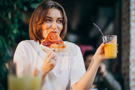 Téléchargez les photos : Jeune jolie femme mangeant de la pizza dans un bar - en image libre de droit