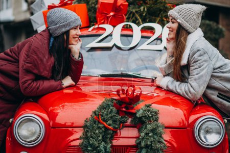 Foto de Dos amigas chicas apoyadas en un coche rojo afuera en invierno - Imagen libre de derechos