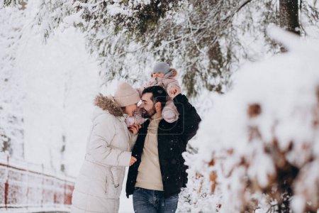 Téléchargez les photos : Jeune famille avec petite fille dans une forêt d'hiver pleine de neige - en image libre de droit