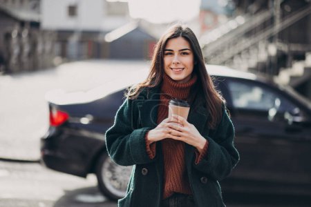 Photo for Young woman drinking coffee by her car - Royalty Free Image