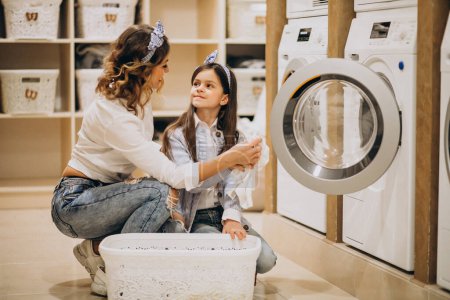 Téléchargez les photos : Mère avec sa fille faisant la lessive à la laverie libre-service - en image libre de droit