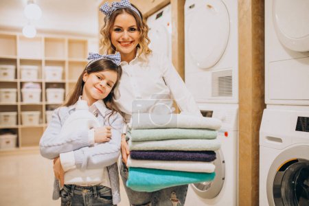 Photo for Mother with daughter doing laundry at self serviece laundrette - Royalty Free Image