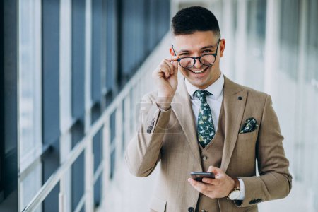 Téléchargez les photos : Jeune homme d'affaires beau debout avec téléphone au bureau - en image libre de droit
