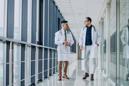 Foto de Dos doctores varones, caminando en la clínica, usando batas blancas de laboratorio - Imagen libre de derechos