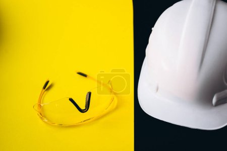 Photo for White hard hat with protection eyeglasses isolated on a black and yellow background - Royalty Free Image