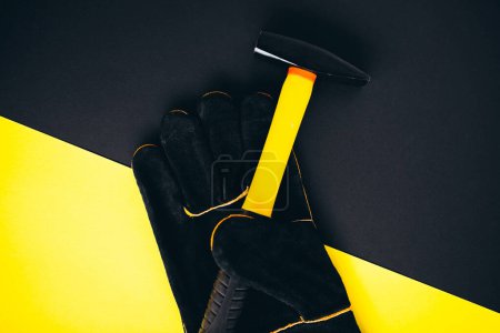 Téléchargez les photos : Gant de travail avec marteau isolé sur fond noir et jaune - en image libre de droit