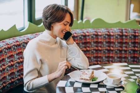 Photo for Young woman eating tiramisu with tea at a cafe - Royalty Free Image