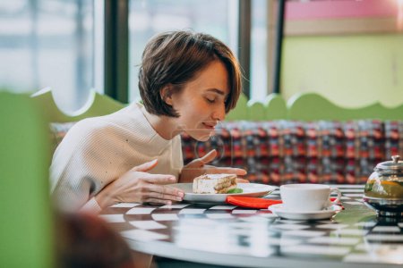 Téléchargez les photos : Jeune femme mangeant du tiramisu avec du thé dans un café - en image libre de droit