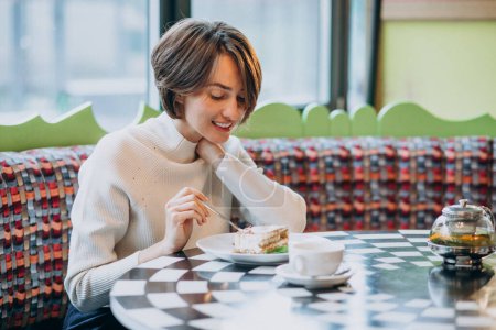 Téléchargez les photos : Jeune femme mangeant du tiramisu avec du thé dans un café - en image libre de droit
