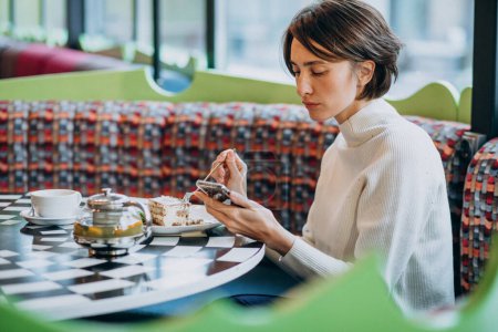 Photo for Young woman eating tiramisu with tea at a cafe - Royalty Free Image