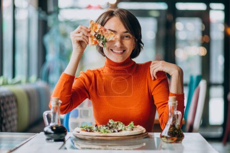Téléchargez les photos : Jeune jolie femme mangeant de la pizza au bar à pizza - en image libre de droit