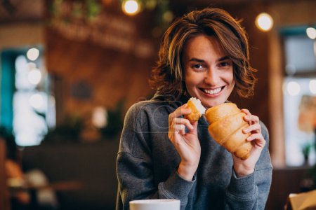 Photo for Young woman eating croissants at a cafe - Royalty Free Image