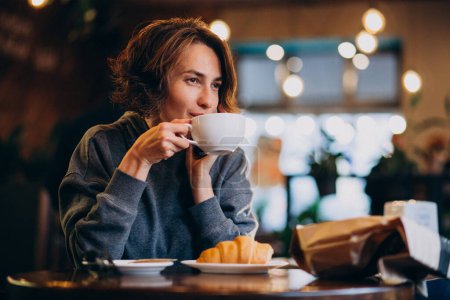 Téléchargez les photos : Jeune femme mangeant des croissants dans un café - en image libre de droit