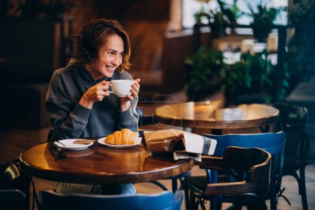 Photo for Young woman eating croissants at a cafe - Royalty Free Image