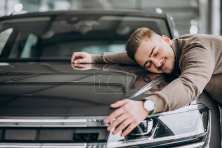 Photo for Young handsome man hugging a car in a car showroom - Royalty Free Image