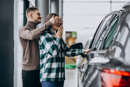Téléchargez les photos : Jeune homme présente une voiture à sa petite amie dans une salle d'exposition de voiture - en image libre de droit
