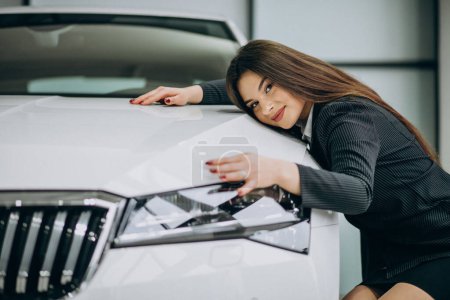 Téléchargez les photos : Jeune femme étreignant une voiture dans un showroom de voiture - en image libre de droit