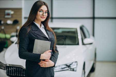 Téléchargez les photos : Jeune vendeuse au carshowroom debout près de la voiture - en image libre de droit