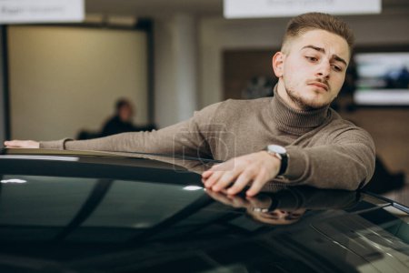 Téléchargez les photos : Jeune homme beau choisir une voiture dans une salle d'exposition de voiture - en image libre de droit