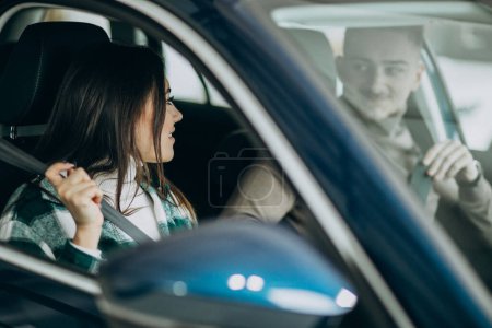 Téléchargez les photos : Jeune couple assis en voiture dans une salle d'exposition de voiture - en image libre de droit