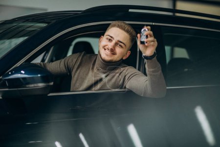 Téléchargez les photos : Jeune homme beau choisir une voiture dans une salle d'exposition de voiture - en image libre de droit