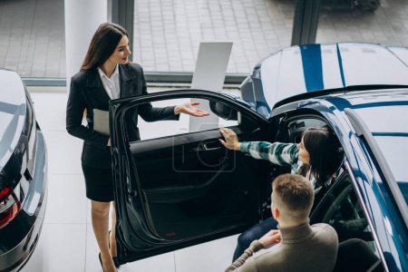 Téléchargez les photos : Jeune couple parlant à un vendeur dans un showroom de voiture - en image libre de droit