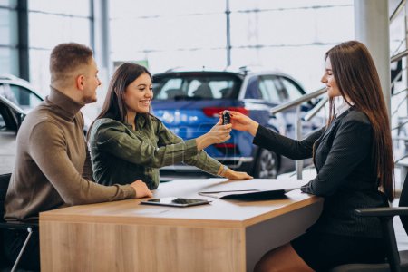 Photo for Young couple talking to a sales person in a car showroom - Royalty Free Image