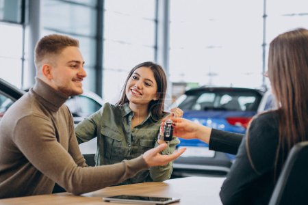 Téléchargez les photos : Jeune couple parlant à un vendeur dans un showroom de voiture - en image libre de droit