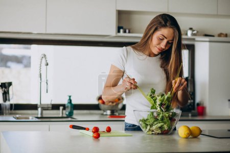 Téléchargez les photos : Jeune femme faisant de la salade à la cuisine - en image libre de droit
