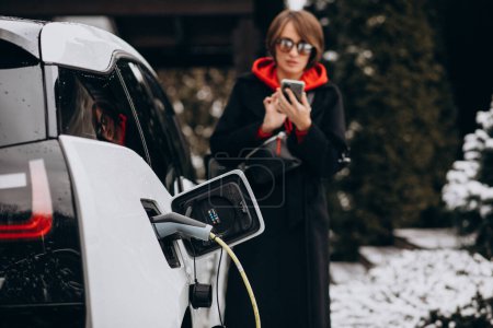 Photo for Woman charging electro car and talking on the phone - Royalty Free Image