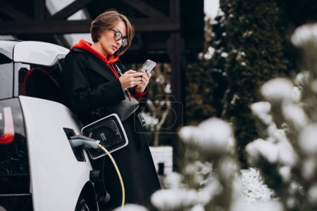 Téléchargez les photos : Femme charge electro voiture et parler au téléphone - en image libre de droit