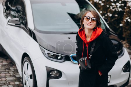 Téléchargez les photos : Femme charge electro voiture par sa maison - en image libre de droit