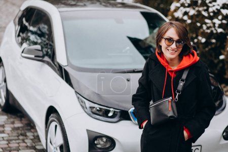 Photo for Woman charging electro car by her house - Royalty Free Image