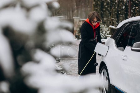 Téléchargez les photos : Femme charge electro voiture par sa maison - en image libre de droit