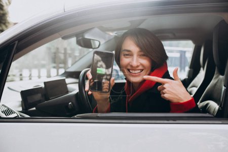 Téléchargez les photos : Femme chargeant sa voiture et regardant le cherger sur son téléphone - en image libre de droit