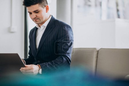 Téléchargez les photos : Jeune homme d'affaires beau travaillant sur ordinateur sur un canapé dans le bureau - en image libre de droit