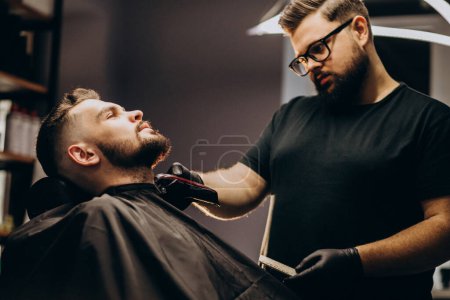 Photo for Handsome man cutting beard at a barber shop salon - Royalty Free Image