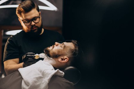 Téléchargez les photos : Beau homme coupant la barbe dans un salon de coiffure - en image libre de droit