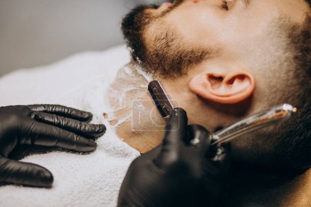 Téléchargez les photos : Beau homme coupant la barbe dans un salon de coiffure - en image libre de droit