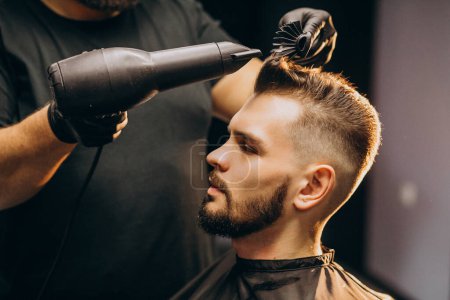 Téléchargez les photos : Beau homme dans un salon de coiffure coiffant les cheveux - en image libre de droit