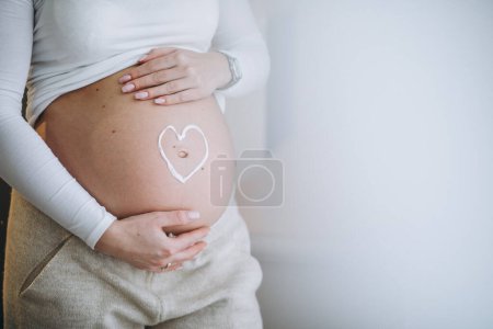 Photo for Pregnant woman applying cream on the belly to prevent stretches - Royalty Free Image