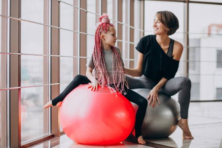 Photo for Mother with little daughter practicing yoga on fit ball by the window - Royalty Free Image