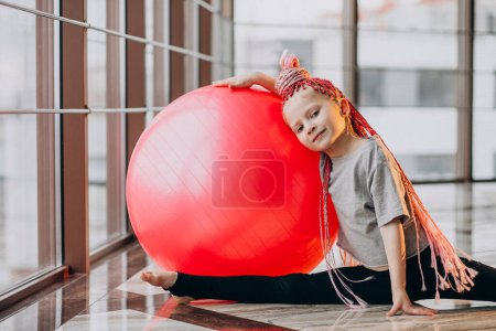 Téléchargez les photos : Petite fille mignonne faisant de la gymnastique avec ballon en studio - en image libre de droit
