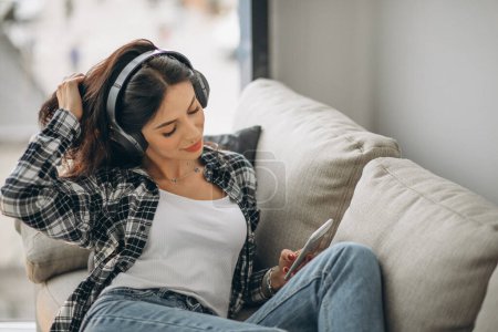 Téléchargez les photos : Jeune femme allongée sur le canapé dans des écouteurs écoutant de la musique - en image libre de droit